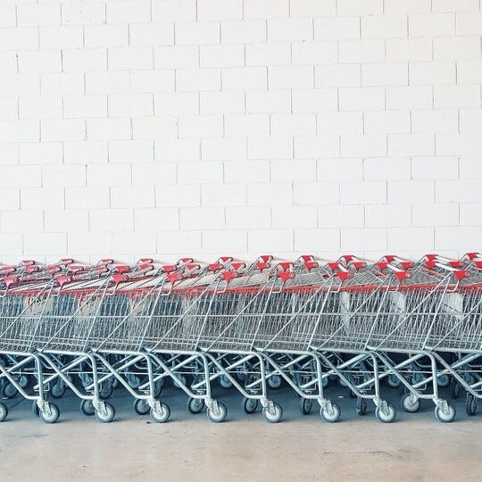 Several shopping carts pushed together and lined up against a white brick wall.