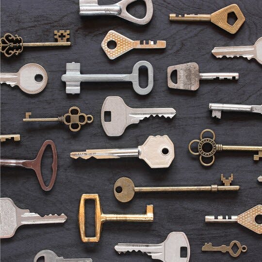 Many different keys placed on a dark wood background.